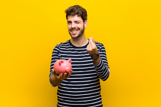 Jovem bonito, segurando um cofrinho contra background laranja