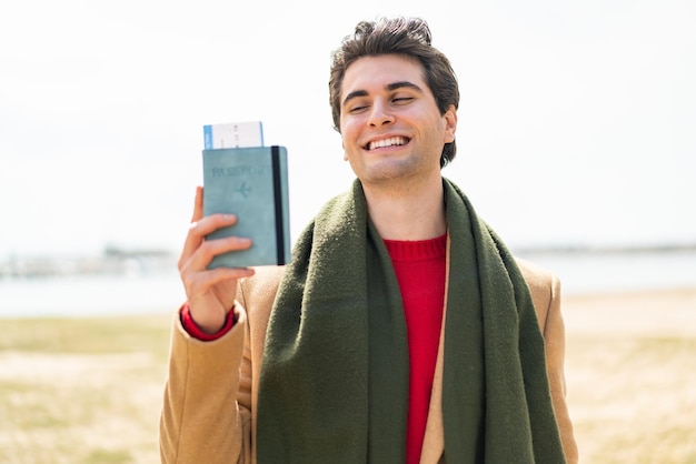 Jovem bonito segurando um passaporte ao ar livre com expressão feliz