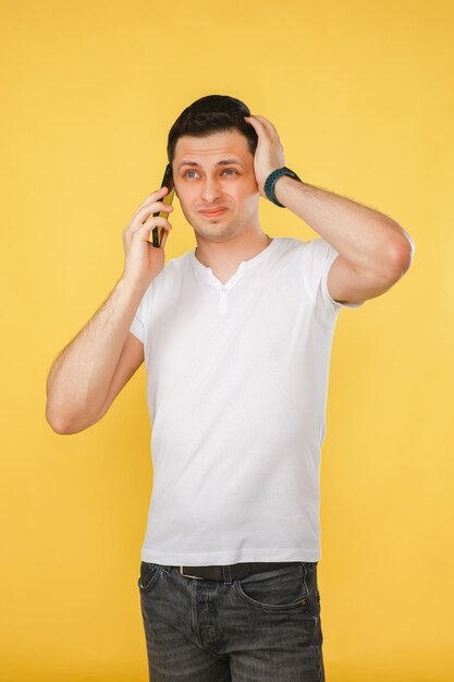 Foto jovem bonito segurando um telefone na mão falando emocionalmente ao telefone em um fundo amarelo liso