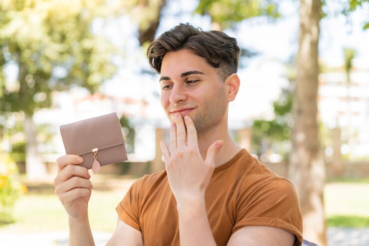 Foto jovem bonito segurando uma carteira e olhando para ela