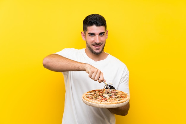 Jovem bonito segurando uma pizza na parede amarela