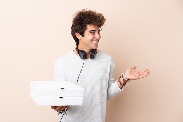 Jovem bonito segurando uma pizza sobre parede isolada com expressão facial de surpresa