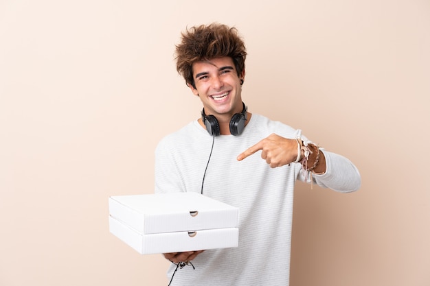 Jovem bonito segurando uma pizza sobre parede isolada e apontando-o