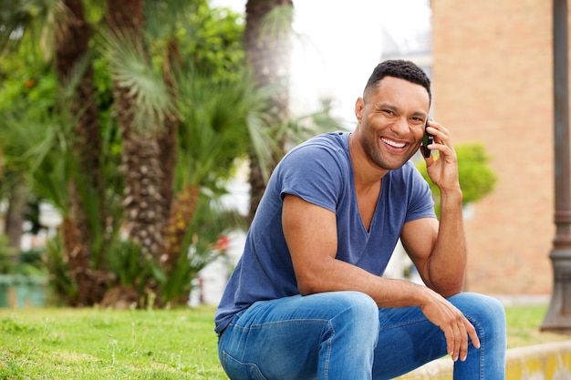 Jovem bonito sentado na calçada e falando no celular