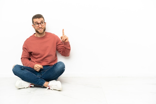 Jovem bonito sentado no chão apontando para cima e surpreso