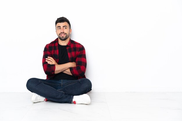 Jovem bonito sentado no chão com os braços cruzados e feliz