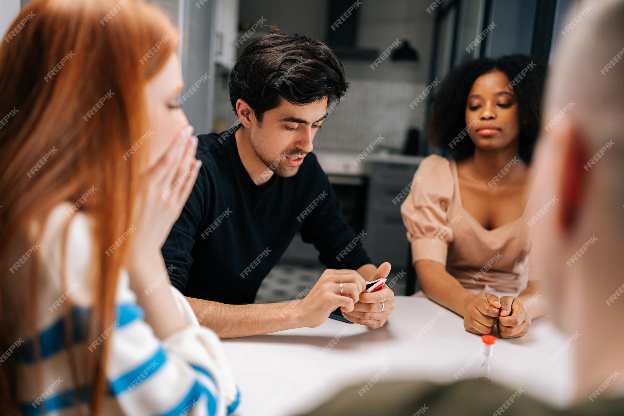 Jovem bonito sério jogando jogos de cartas divertidos contando associações  para diversos amigos desfrutando de atividade de passatempo sentado à mesa  em casa