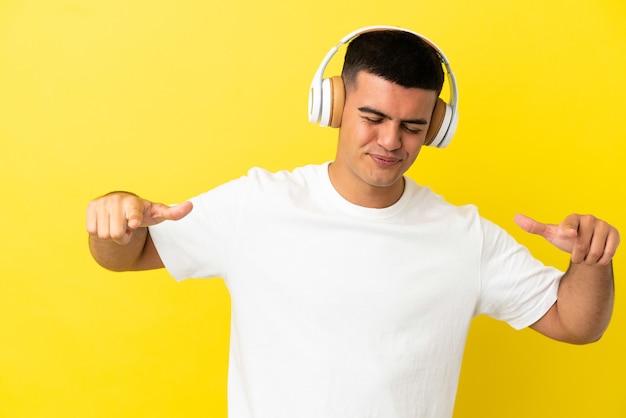 Jovem bonito sobre fundo amarelo isolado ouvindo música e dançando