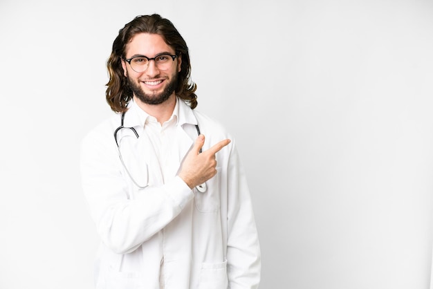 Jovem bonito sobre fundo branco isolado, vestindo um vestido de médico e apontando o lado