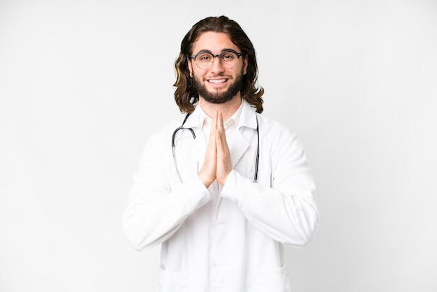 Jovem bonito sobre fundo branco isolado, vestindo uma bata de médico e implorando