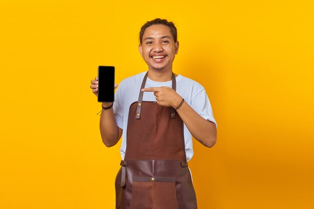 Jovem bonito sorridente apontando para a tela do smartphone em branco sobre fundo amarelo