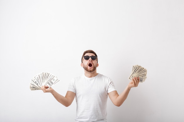 Jovem bonito sorridente com uma barba em uma camisa branca, segurando um monte de notas de cem dólares. dinheiro