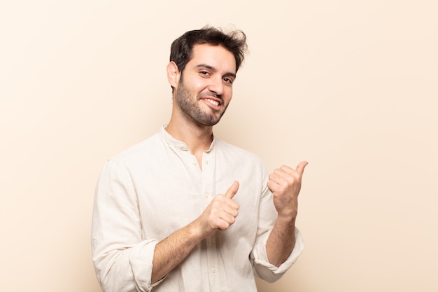 Jovem bonito sorrindo alegre e casualmente apontando para uma cópia do espaço ao lado, sentindo-se feliz e satisfeito