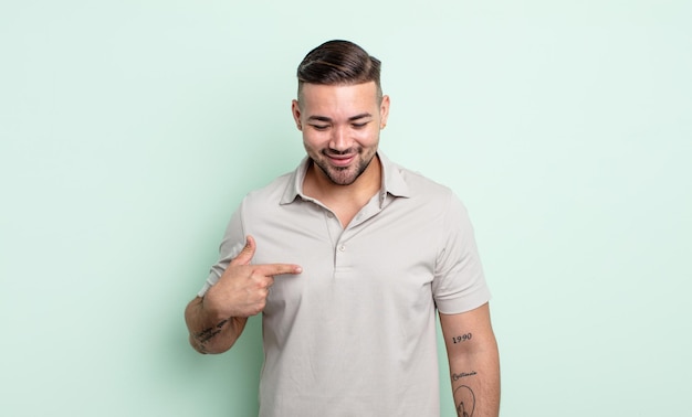 Foto jovem bonito sorrindo alegre e casualmente, olhando para baixo e apontando para o peito