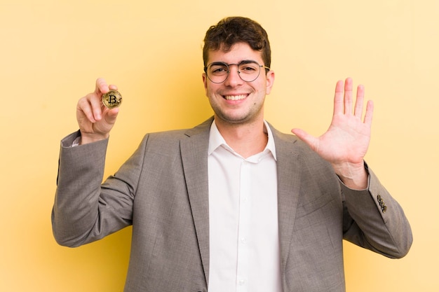 Jovem bonito sorrindo alegremente acenando com a mão dando as boas-vindas e cumprimentando seu conceito de bitcoin