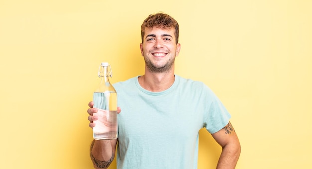 Jovem bonito sorrindo alegremente com uma mão no quadril e confiante. conceito de água