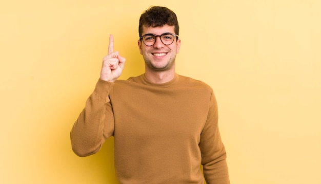 Jovem bonito sorrindo alegremente e alegremente apontando para cima com uma mão para copiar o espaço