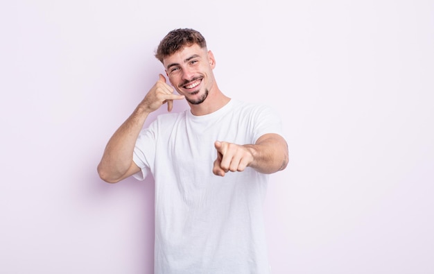 Jovem bonito sorrindo alegremente e apontando para a câmera enquanto faz uma ligação para você mais tarde, falando ao telefone