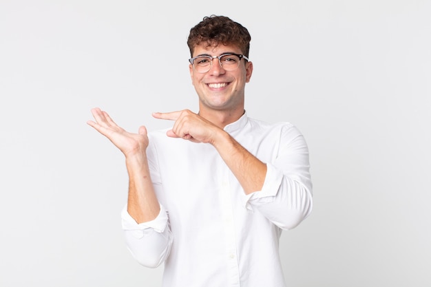 Jovem bonito sorrindo alegremente e apontando para copiar o espaço na palma da mão ao lado, mostrando ou anunciando um objeto