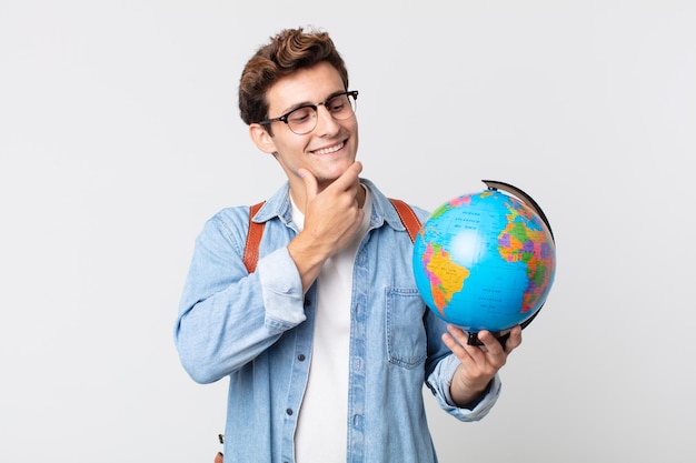 Jovem bonito sorrindo alegremente e sonhando acordado ou duvidando. estudante segurando um mapa do globo do mundo