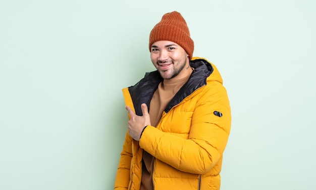 Jovem bonito sorrindo alegremente, sentindo-se feliz e apontando para o lado. conceito de clima frio