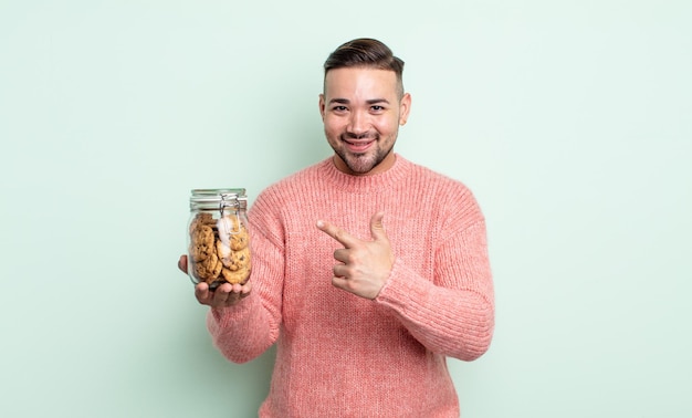 Jovem bonito sorrindo alegremente, sentindo-se feliz e apontando para o lado. conceito de garrafa de biscoitos