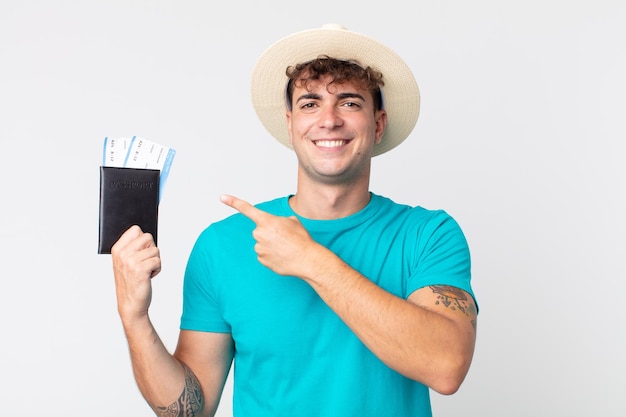 Jovem bonito sorrindo alegremente, sentindo-se feliz e apontando para o lado. viajante segurando seu passaporte