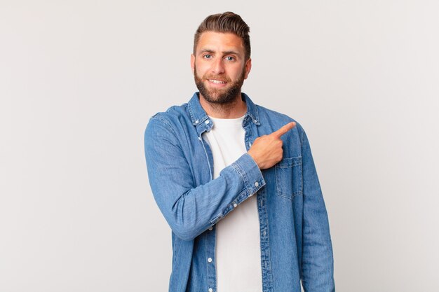 Jovem bonito sorrindo alegremente, sentindo-se feliz e apontando para o lado