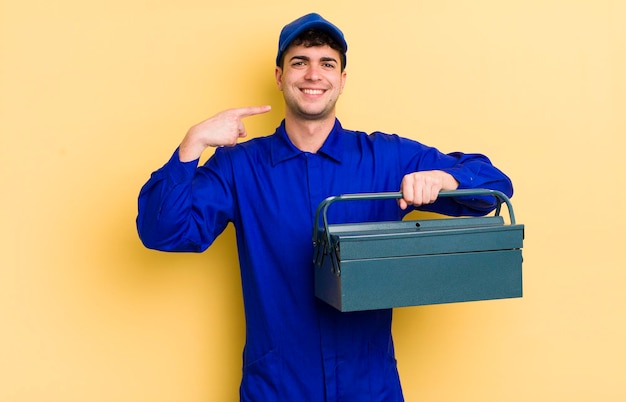 Jovem bonito sorrindo com confiança apontando para o próprio conceito de encanador de sorriso largo