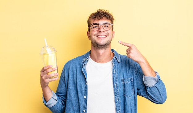 Jovem bonito sorrindo com confiança, apontando para o próprio sorriso largo. conceito de milkshake