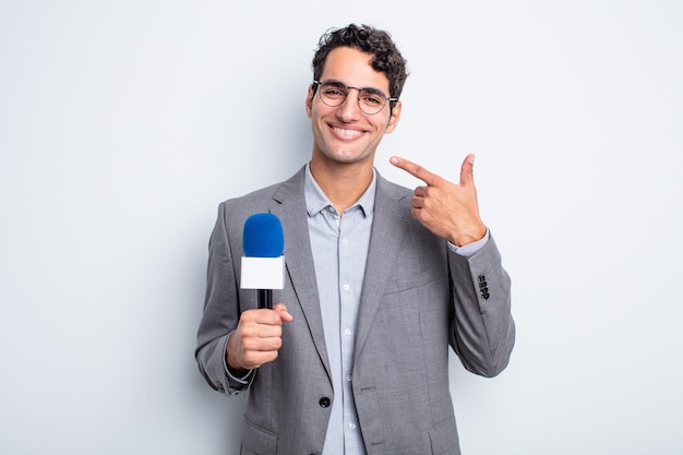 Jovem bonito sorrindo com confiança apontando para próprio sorriso largo. apresentador com microfone