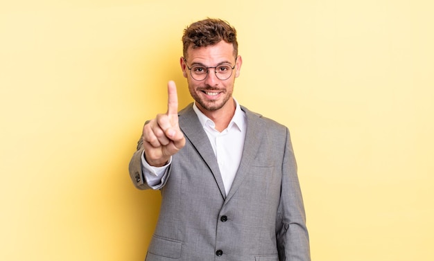 Jovem bonito sorrindo com orgulho e com confiança, fazendo o número um. conceito de negócios