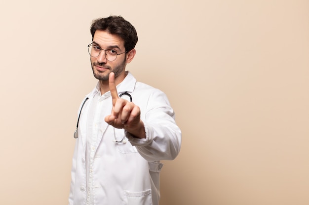 Jovem bonito sorrindo com orgulho e confiança fazendo a pose número um triunfantemente, sentindo-se um líder