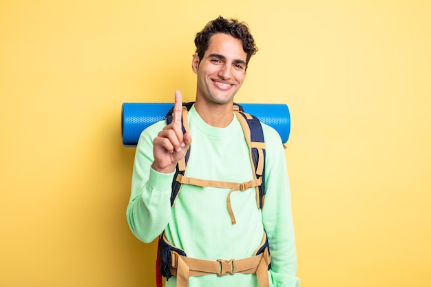 Jovem bonito sorrindo com orgulho e confiança fazendo o número um