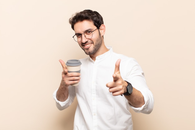 Jovem bonito sorrindo com uma atitude positiva, bem-sucedida e feliz apontando para a câmera, fazendo sinal de arma com as mãos