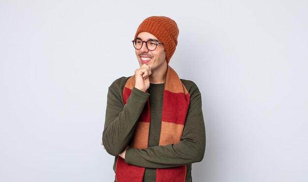 Jovem bonito sorrindo com uma expressão feliz e confiante com a mão no queixo. conceito de roupas de inverno