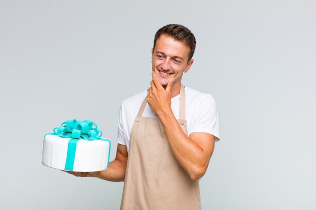 Jovem bonito sorrindo com uma expressão feliz e confiante com a mão no queixo, pensando e olhando para o lado