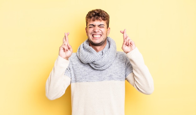 Jovem bonito sorrindo e cruzando ansiosamente os dois dedos, sentindo-se preocupado e desejando ou esperando boa sorte