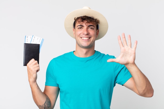 jovem bonito sorrindo e parecendo amigável, mostrando o número cinco. viajante segurando seu passaporte