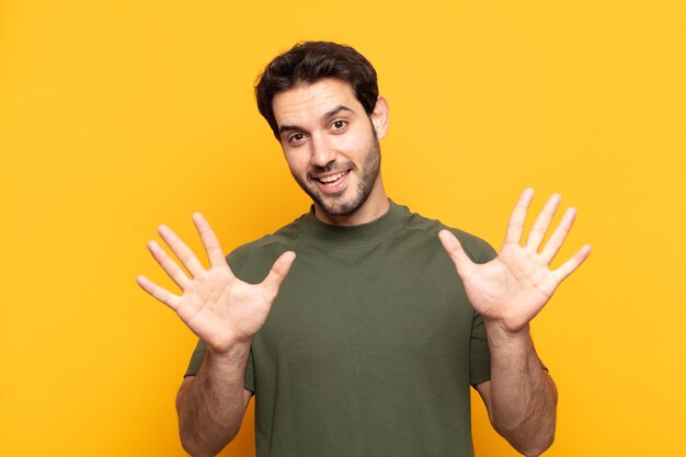 Jovem bonito sorrindo e parecendo amigável, mostrando o número dez ou décimo com a mão para a frente, em contagem regressiva