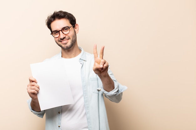 Jovem bonito sorrindo e parecendo amigável, mostrando o número dois ou o segundo com a mão para a frente, em contagem regressiva