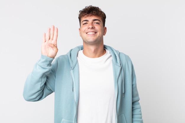 jovem bonito sorrindo e parecendo amigável, mostrando o número quatro ou o quarto com a mão para a frente, em contagem regressiva