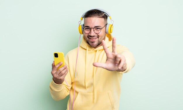 Jovem bonito sorrindo e parecendo amigável, mostrando o número três. conceito de fones de ouvido e smartphone