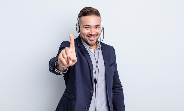 Jovem bonito sorrindo e parecendo amigável, mostrando o número um. conceito de teleartista