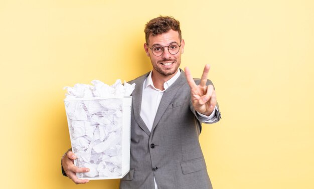 Jovem bonito sorrindo e parecendo feliz, gesticulando vitória ou paz bolas de papel conceito de lixo