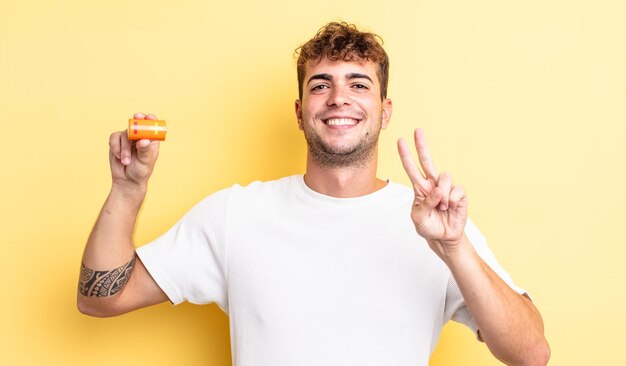 Jovem bonito sorrindo e parecendo feliz, gesticulando vitória ou paz com uma bateria