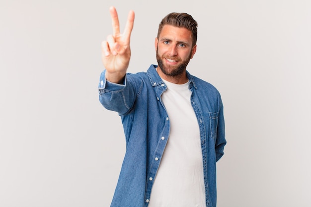 Jovem bonito sorrindo e parecendo feliz, gesticulando vitória ou paz