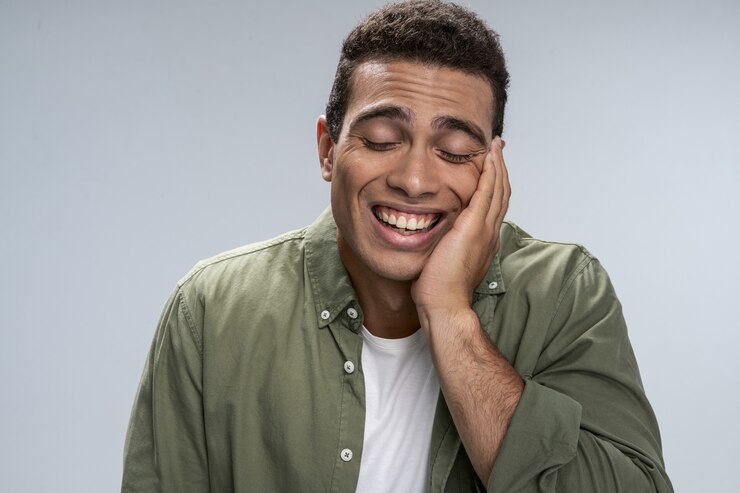 Jovem bonito sorrindo fechando os olhos e segurando a mão sob o queixo