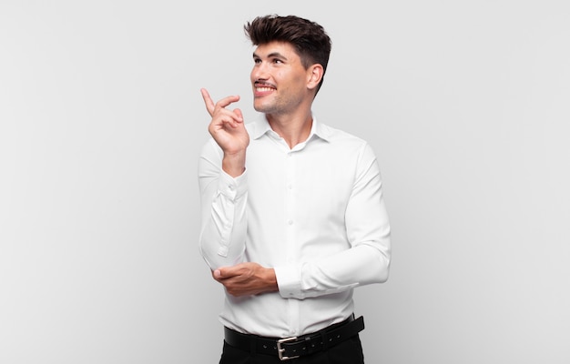 Jovem bonito sorrindo feliz e olhando de soslaio, imaginando, pensando ou tendo uma ideia