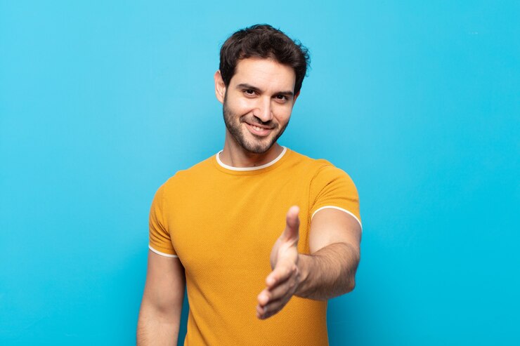 Foto jovem bonito sorrindo, parecendo feliz, confiante e amigável, oferecendo um aperto de mão para fechar um negócio, cooperando